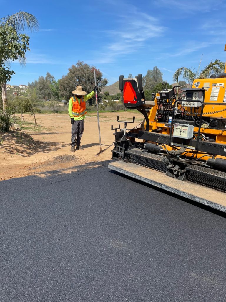 A worker is smoothing asphalt with a machine nearby